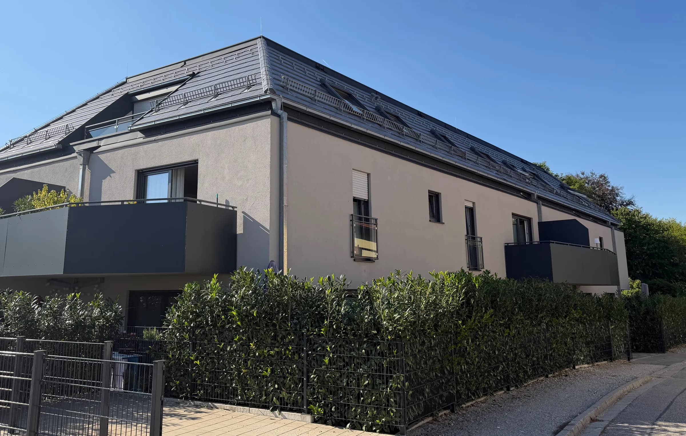 Wohnanlage mit hellgrau verputzter Fassade, dunklen Balkonen und Hecke